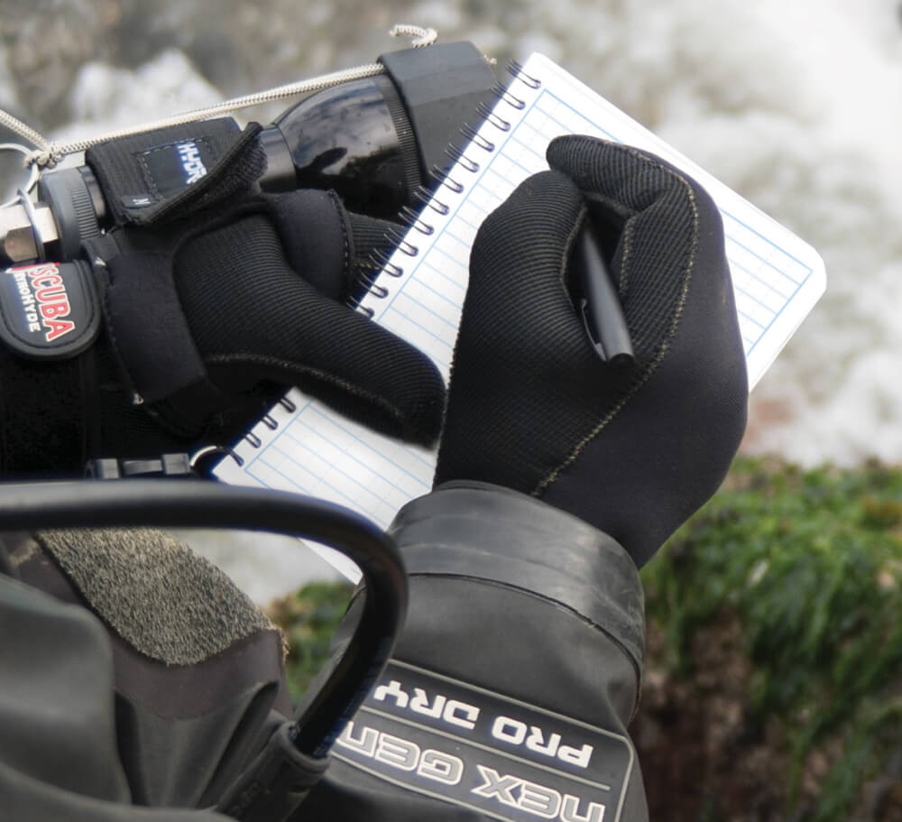 Scuba diver writing in a waterproof notebook with a weatherproof pen.