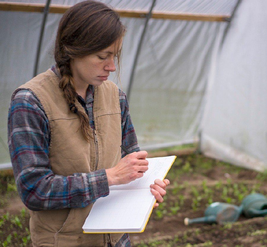 Anika writing down her crop plans in a green house.