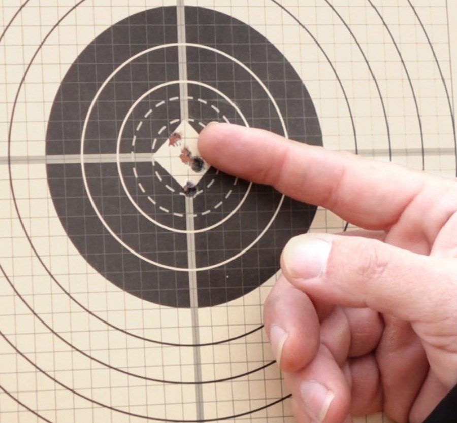 Ash pointing to bullet holes through an all weather target.