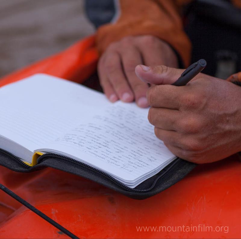 Kayaker writing in a hard cover book with an weatherproof pen.