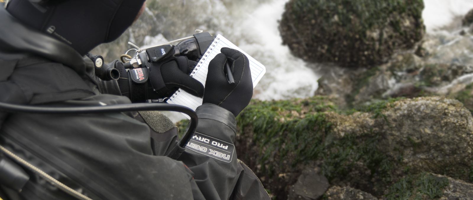 Scuba diver and vessel inspector writing in notebook with weatherproof pen.