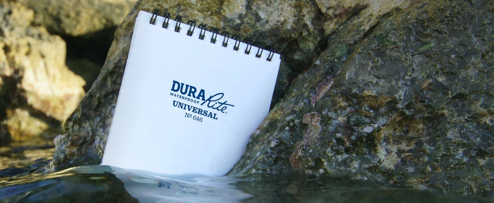 DuraRite Spiral notebook siting in water against a rock.