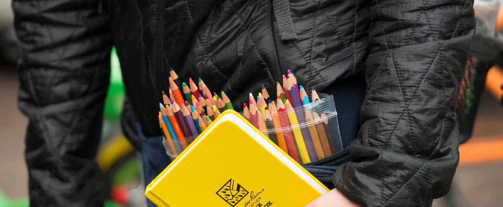 Artist holding hard cover book near assortment of colored pencils