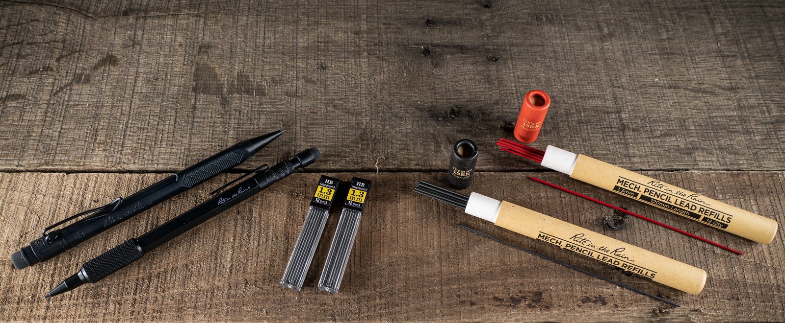 No. 13 and 15 pencils with dark and red lead refill tubes laying on wood.