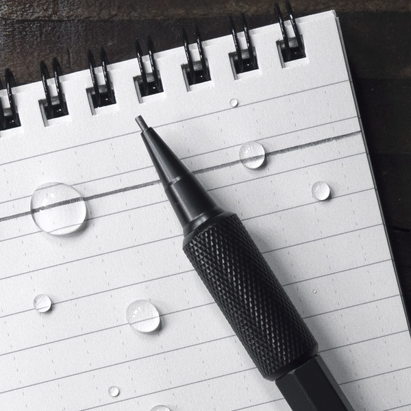 Mechanical pencil resting on notebook with writting through water drops.