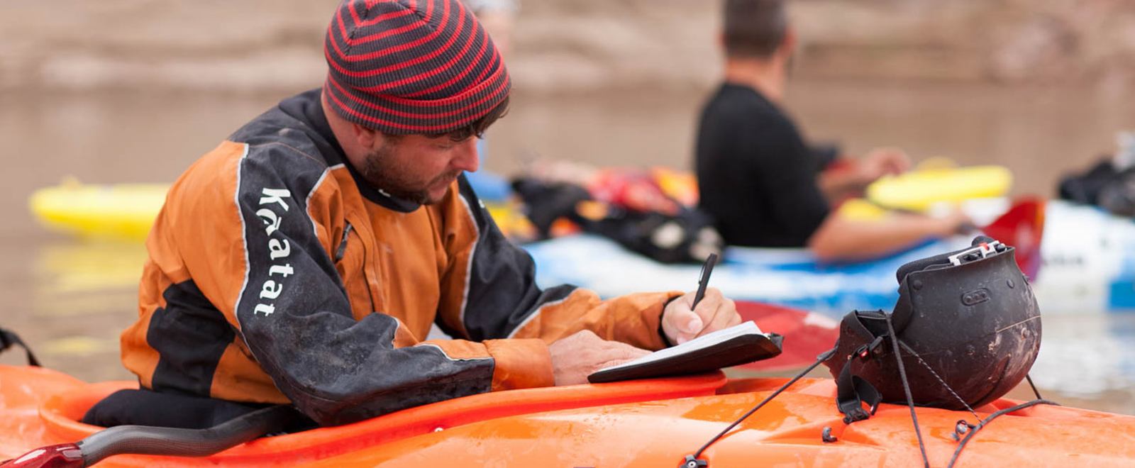 A Kayaker, using the cockpit rim, writes in his Rite in the Rain book with a weatherproof pen.