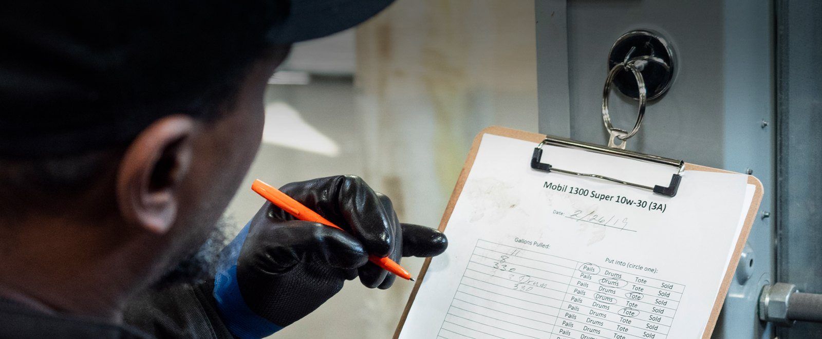 Person in a fuel transport warehouse, writing on weatherproof printer paper, using an all-weather pen.