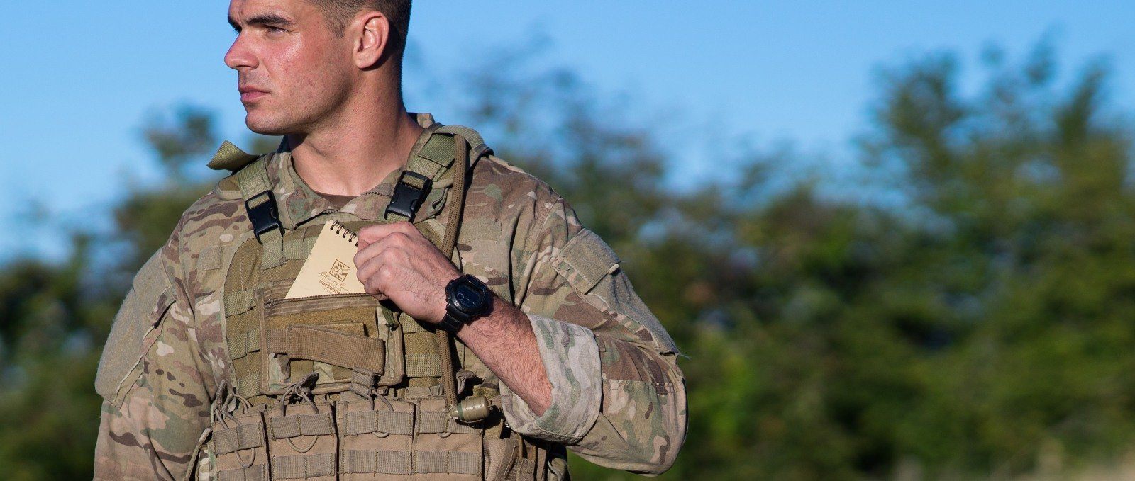 Person in the armed forces putting a top spiral notebook into his uniform's pocket.