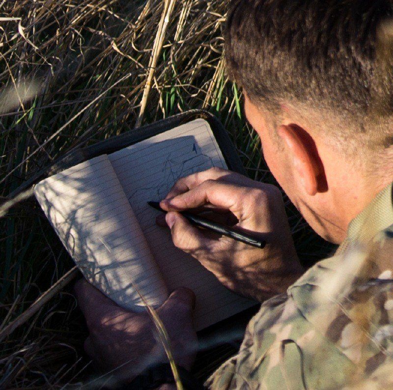 Person in armed forces writing in a tactical field book with an all weather pen.