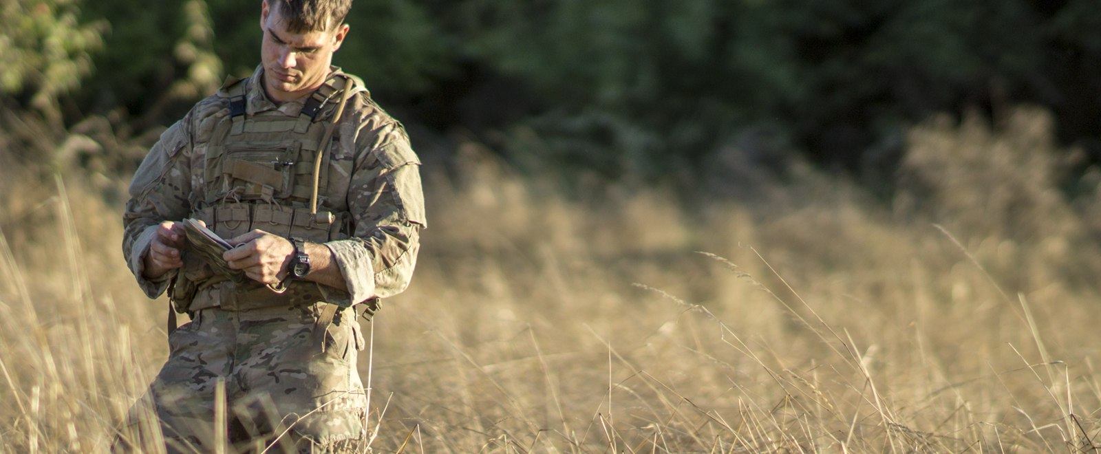 Person in the armed forces holding a multicam cover and field book.