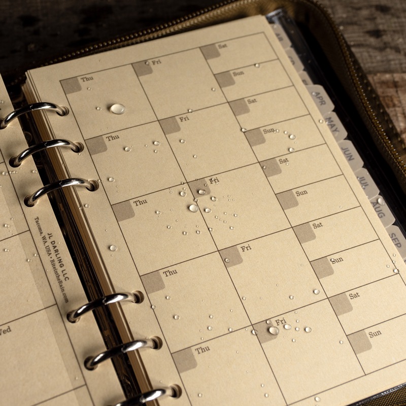 Planner open to wet daily planner loose leaf, weatherproof pen sitting on pages.